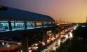 Nighttime in Delhi, highlighting the bustling traffic on the road with the metro gliding above the illuminated city
